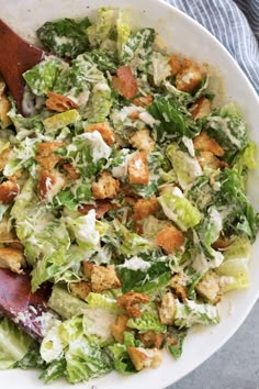 a salad with lettuce, carrots and dressing in a white bowl next to a wooden spoon