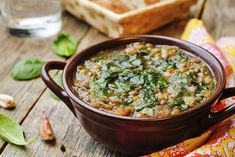 a brown bowl filled with soup on top of a wooden table next to bread and green leaves