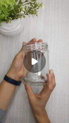 two hands holding a glass jar with water in it on top of a table next to a potted plant