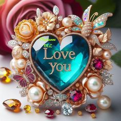 a heart shaped brooch with the words i love you surrounded by jewels and flowers