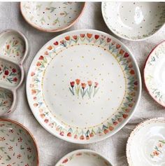 many plates and bowls are laid out on a tablecloth with flowers painted on them