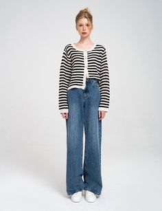 a woman standing in front of a white background wearing blue jeans and a striped sweater