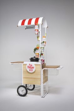 an outdoor food cart with potted plants on the top and red and white striped awning