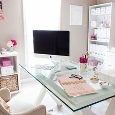 a glass desk topped with a computer monitor next to a white chair and book shelf