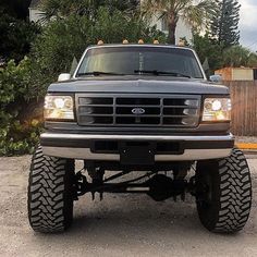 the front end of a pickup truck parked in a driveway with trees and bushes behind it