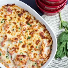 a casserole dish with cheese and spinach leaves on the table next to it