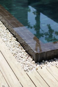 a wooden deck next to a pool with rocks and stones around it, along with a water feature