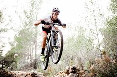 a man riding a bike up the side of a tree covered hill in dirt and grass