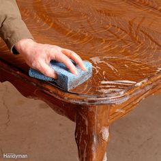 a person with a sponge on top of a wooden table in the process of cleaning