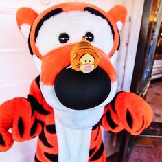 a stuffed animal is holding a ball in its mouth and wearing an orange tiger costume