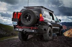 a black jeep parked on top of a rocky hill under a cloudy sky with mountains in the background