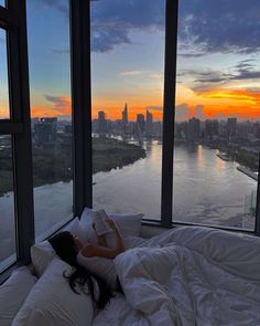 a woman is laying in bed looking out the window at the river and cityscape