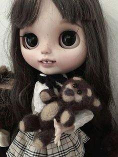 a close up of a doll holding a teddy bear with big eyes and long hair