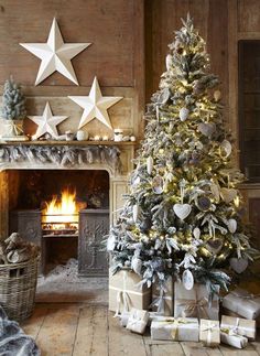 a decorated christmas tree in front of a fire place with white stars on the wall