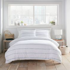 a bed with white and blue striped comforter in a bedroom next to a window