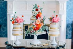 three tiered wedding cake with flowers on top and gold trim around the edges, sitting on a table in front of a fireplace