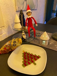 an elf is sitting on the table next to a plate with gummy bears in it