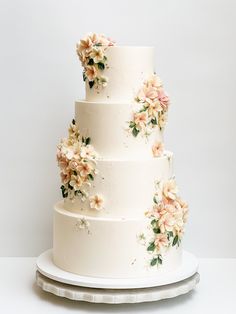 a three tiered wedding cake with flowers on the top and bottom, sitting on a white platter