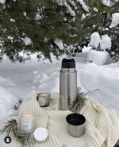 thermos and candles are sitting on a blanket in the snow near pine trees