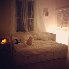 a dog sitting on top of a white bed in a bedroom next to a window