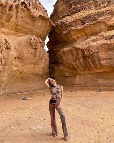 a woman standing in the middle of a desert with her hands on her head and wearing boots