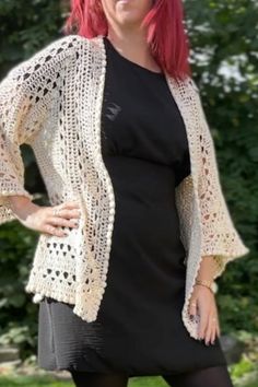 a woman with red hair wearing a black dress and white crochet cardigan