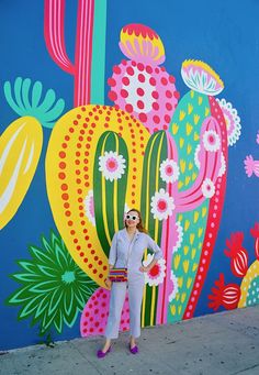 a woman standing in front of a colorful wall with flowers and cacti on it