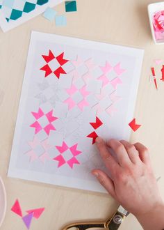 someone cutting out paper stars on a piece of white paper with pink and blue cut outs