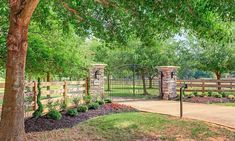 a gated in area with trees and flowers on the ground near a walkway that leads to a grassy field