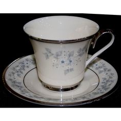 a white cup and saucer with blue flowers on the rim, sitting on a black surface