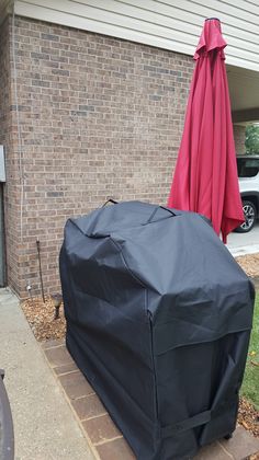 an outdoor bbq grill cover sitting on the side of a building next to a red umbrella