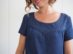 a woman in a blue dress smiling at the camera with her hair pulled back and wearing a gold necklace