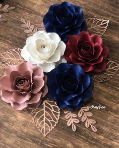 four paper flowers with leaves on top of a wooden table next to scissors and thread