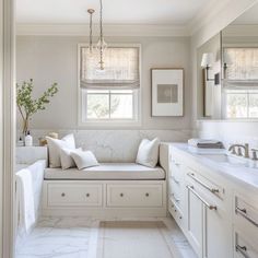 a white bathroom with marble counter tops and large window seat in the corner between two sinks