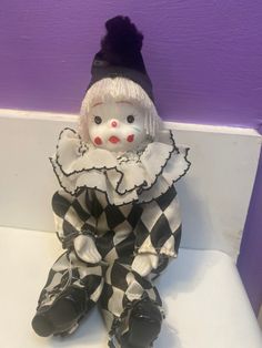 a small white and black clown doll sitting on a shelf next to a purple wall