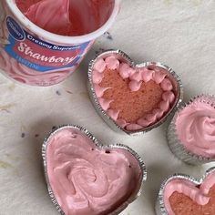 three heart shaped cupcakes with pink frosting next to a container of ice cream