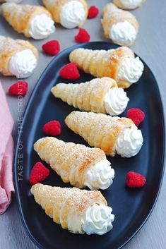 small pastries with whipped cream and raspberries on a black plate