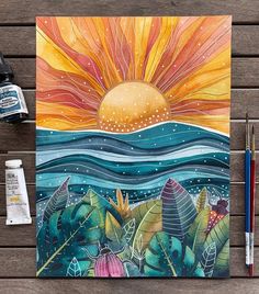 a painting on a wooden table next to paint supplies and watercolor pens, with the sun in the background