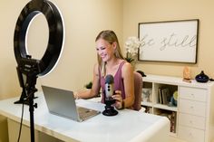 a woman sitting at a desk with a laptop and microphone in front of her computer