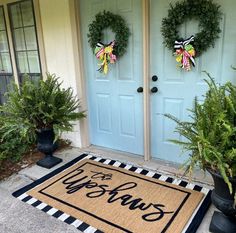 two wreaths on the front door of a house with welcome mats and potted plants