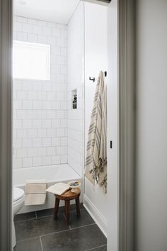 a bathroom with a white toilet sitting next to a walk in shower and a wooden stool