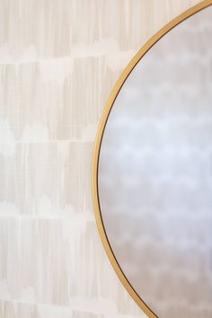 a round mirror hanging on the wall next to a white and beige wallpapered wall