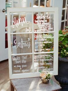 an old window with menus on it and flowers in the vase next to it