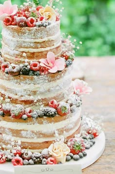 a multi layer cake with flowers and berries on the top is sitting on a plate