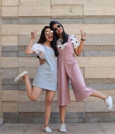 two women posing for the camera in front of a wall