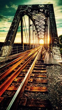 the sun is setting on an old train track crossing over a bridge that crosses into another country