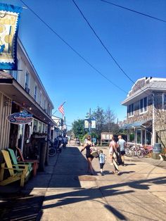 people walking down the sidewalk in front of shops and stores on a sunny day with blue skies