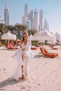 a woman standing on top of a sandy beach next to white umbrellas and palm trees