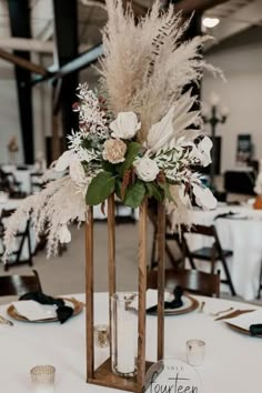 an arrangement of flowers and greenery in a vase on top of a white table cloth