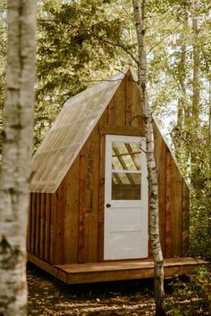 a small cabin in the woods with a white door and window on it's side